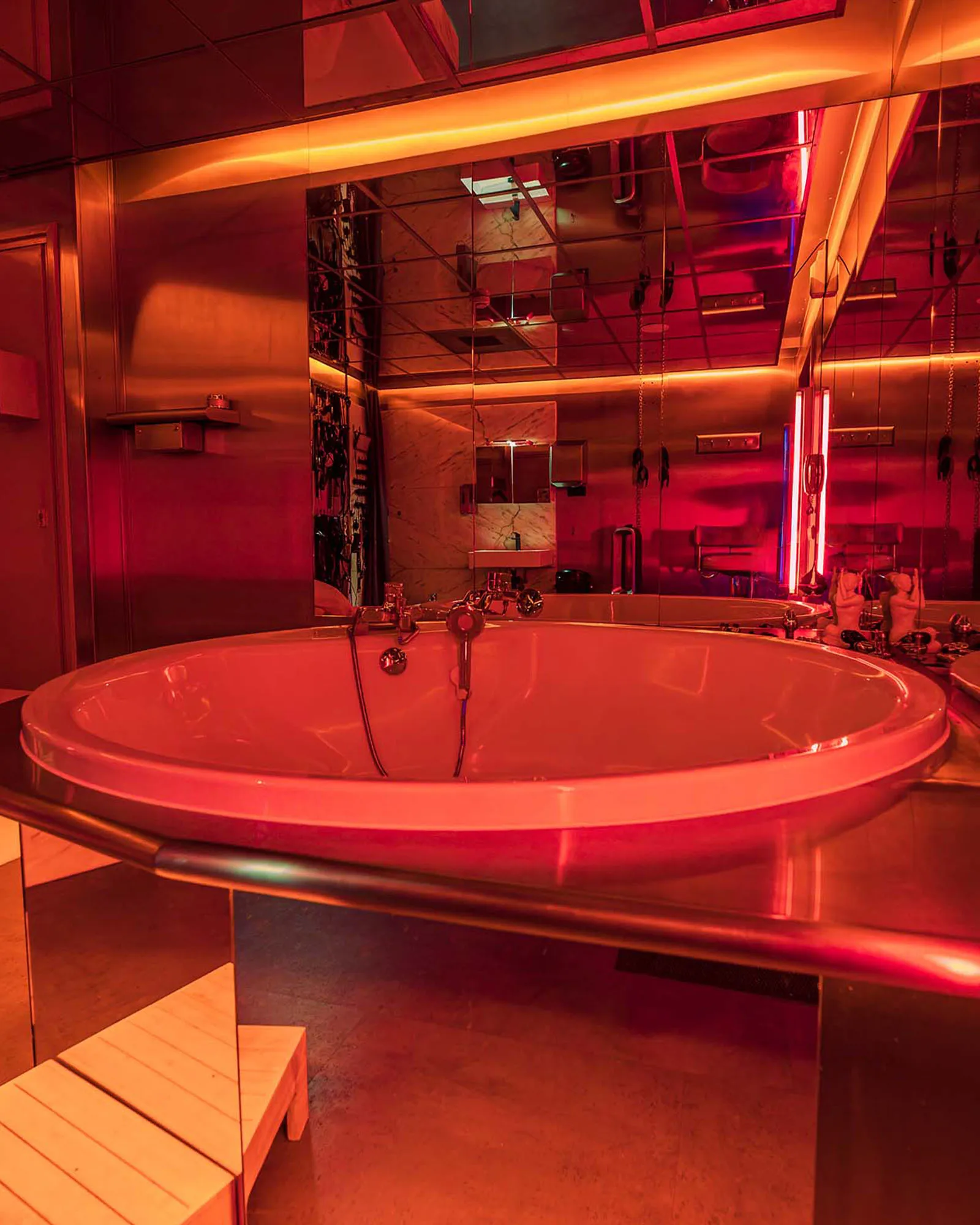 Het ronde bubbelbad in een kamer met spiegelwanden en rood neonlicht, met aan de wand materiaal voor SM.