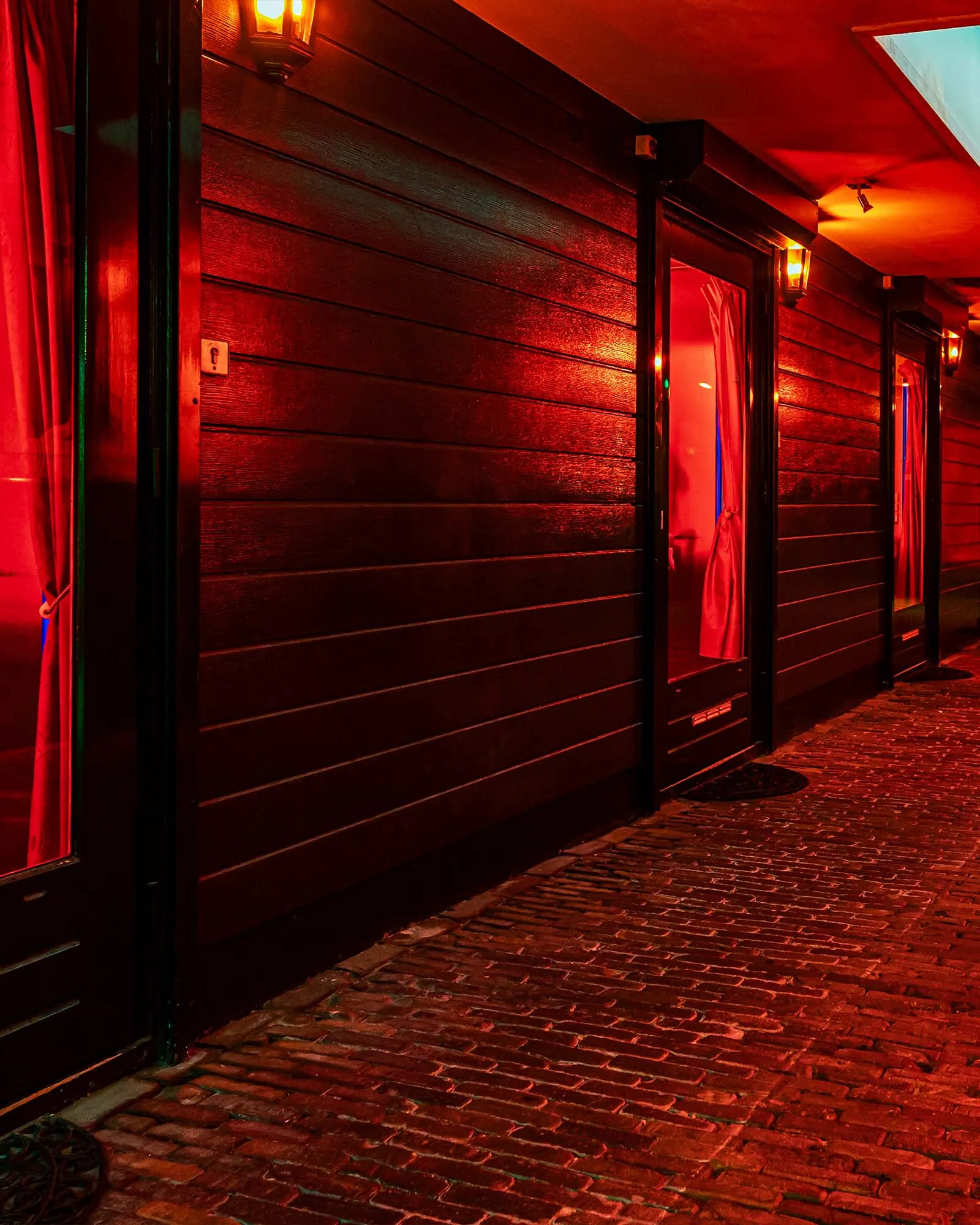 De gang langs de kamers in rood licht, met lantaarns en deuren met rode gordijnen.